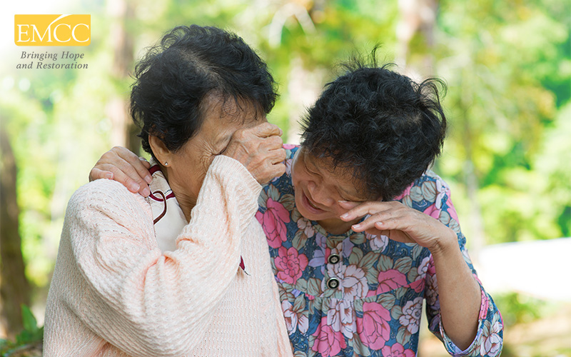 Two older individuals sharing emotional moment outdoors.
